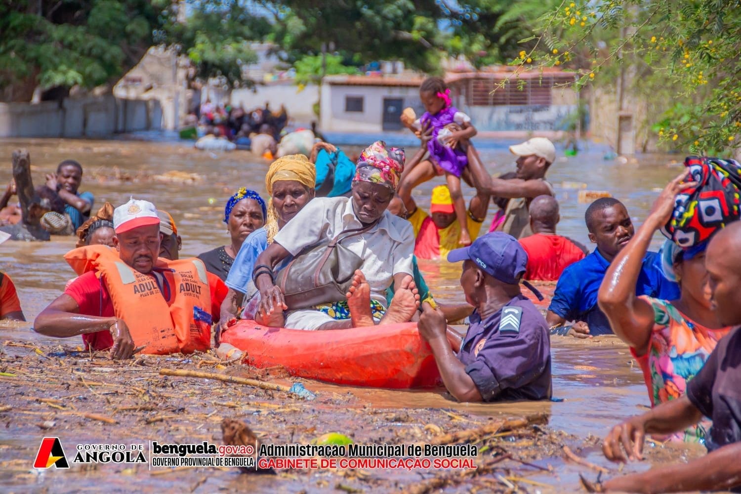Bombeiros e policias a ajudar senhoras a atravessar aguas da inundacao em Benguela, com outras pessoas com agua ate ao peito ao lado
